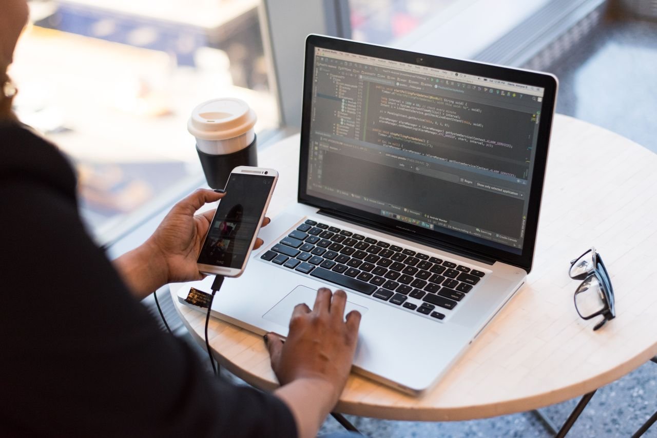 Services Developer working remotely, coding on a laptop with phone in hand, showcasing modern work culture.