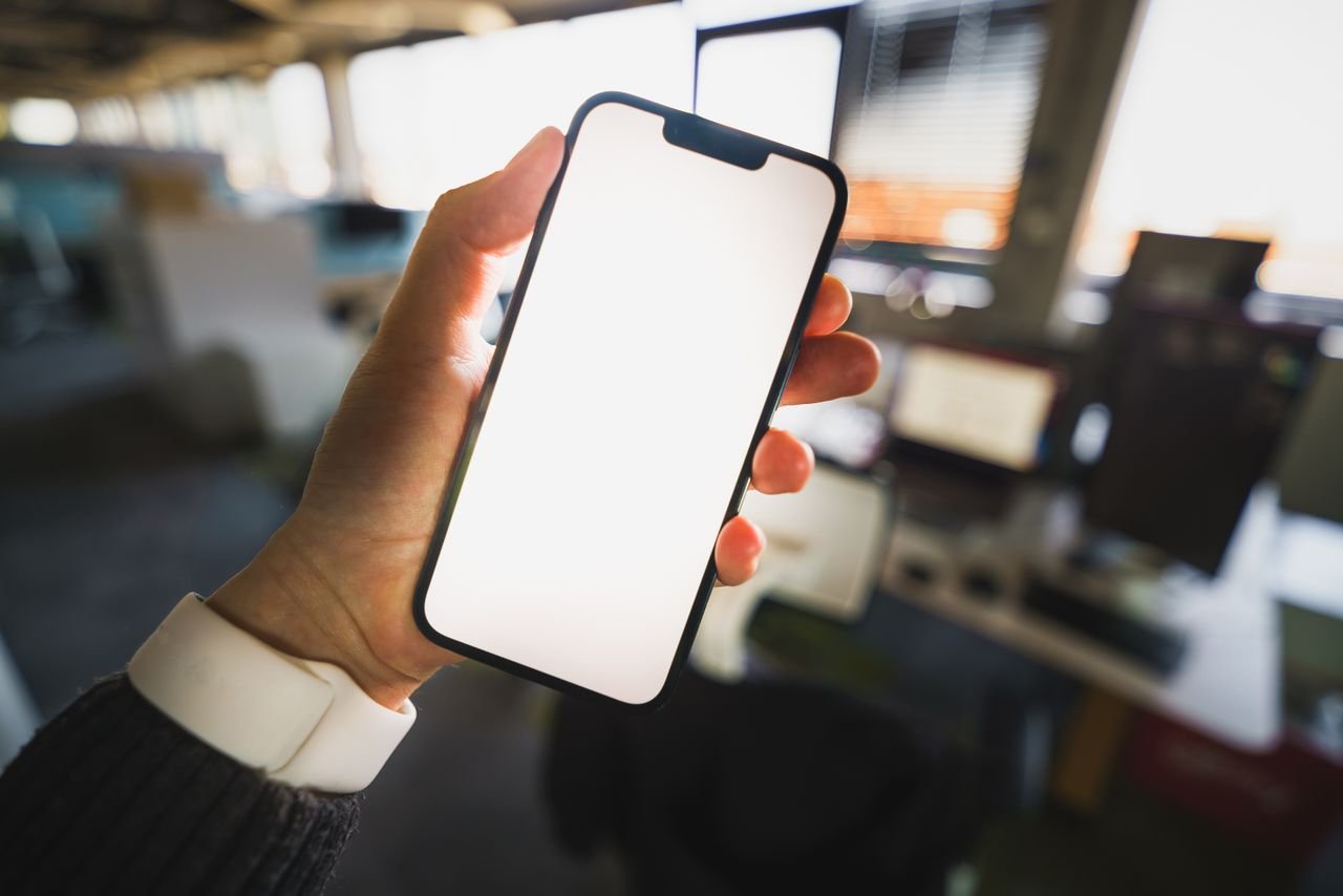 About A blank smartphone screen held in an office environment, perfect for mockup presentations.