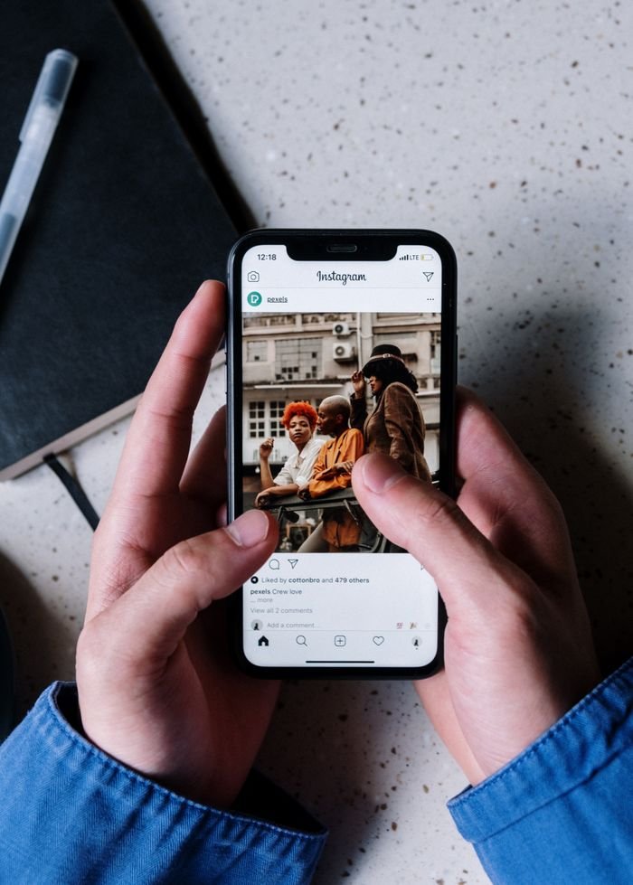 About Close-up of hands holding a smartphone browsing Instagram with a notebook and pen nearby.