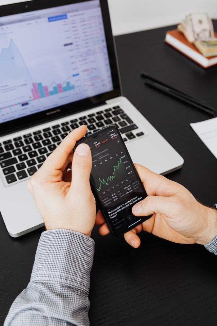 Services Close-up of hands examining stock market graphs on smartphone and laptop.