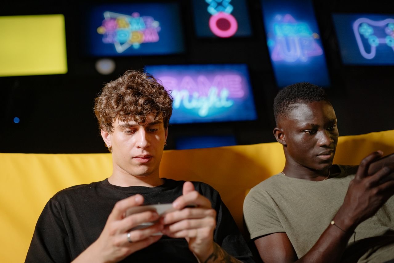Services Two friends play mobile games indoors, focusing intently on their smartphones.